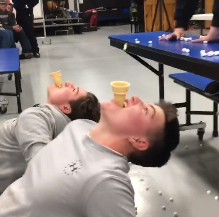 Two students positioned on the floor face up with empty ice cream cones in their mouth waiting for marshmallows to fall in.